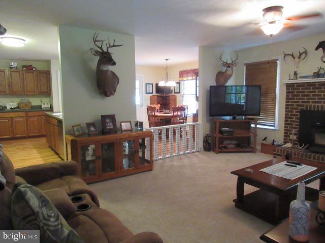 living room featuring ceiling fan with notable chandelier, light colored carpet, and a fireplace