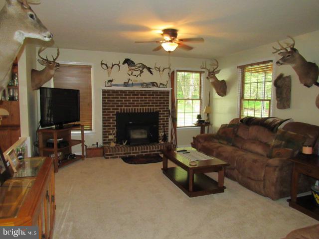 carpeted living room with a brick fireplace and ceiling fan