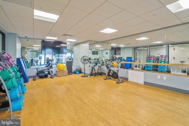 exercise room with light hardwood / wood-style floors and a paneled ceiling