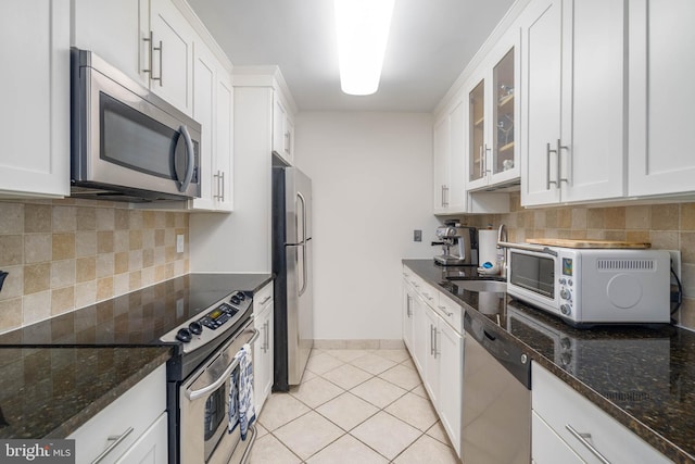 kitchen with dark stone countertops, white cabinetry, backsplash, light tile patterned floors, and stainless steel appliances