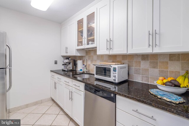 kitchen featuring dark stone countertops, tasteful backsplash, white cabinets, light tile patterned floors, and stainless steel appliances