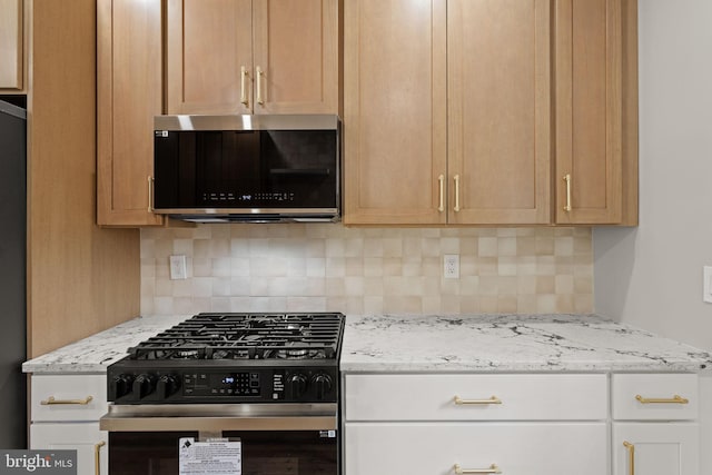 kitchen featuring light stone countertops, gas stove, decorative backsplash, and fridge