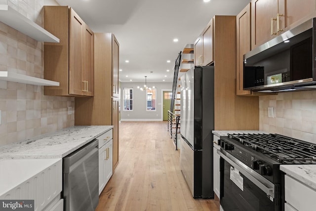 kitchen featuring a notable chandelier, stainless steel appliances, light stone countertops, decorative backsplash, and light hardwood / wood-style floors