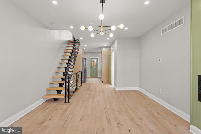 unfurnished living room featuring a notable chandelier and light hardwood / wood-style flooring