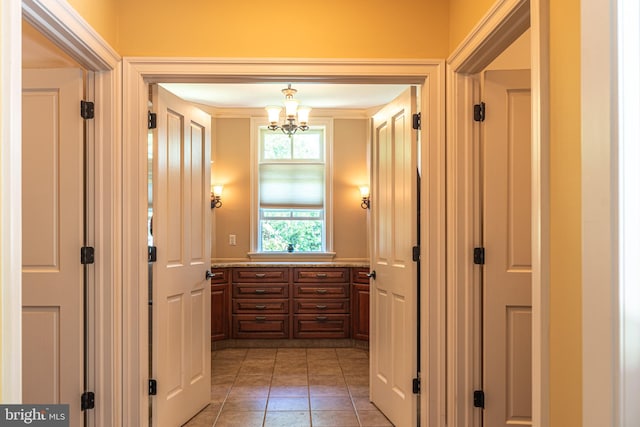 corridor featuring crown molding, light tile patterned floors, and a notable chandelier