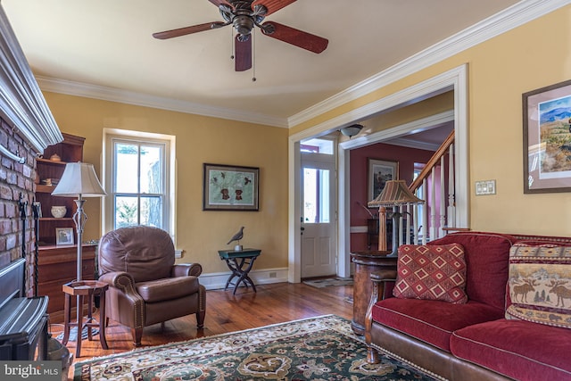 living room with a brick fireplace, ceiling fan, hardwood / wood-style floors, and crown molding