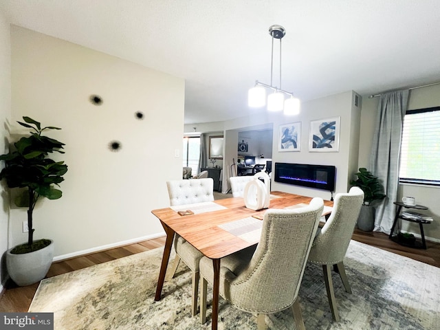 dining room featuring a glass covered fireplace, wood finished floors, and baseboards