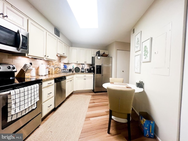 kitchen featuring tasteful backsplash, light wood-style flooring, appliances with stainless steel finishes, a skylight, and white cabinets