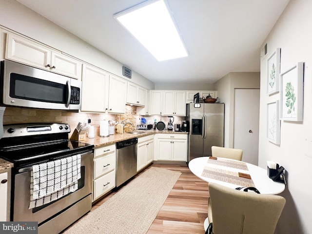 kitchen with light stone counters, tasteful backsplash, light hardwood / wood-style flooring, white cabinetry, and appliances with stainless steel finishes