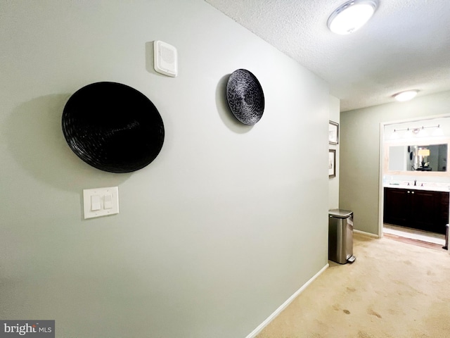 hallway with light colored carpet, a textured ceiling, baseboards, and a sink