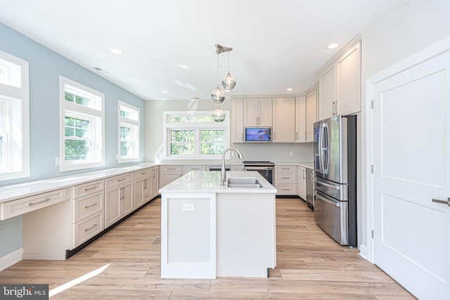 kitchen with an island with sink, stainless steel appliances, pendant lighting, and light wood-type flooring