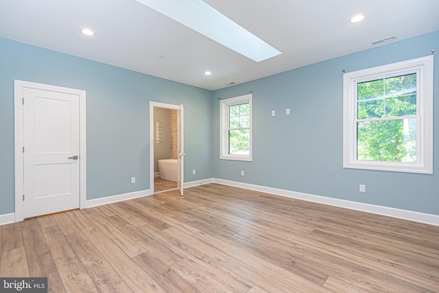 unfurnished bedroom featuring light wood-type flooring, ensuite bath, and a skylight