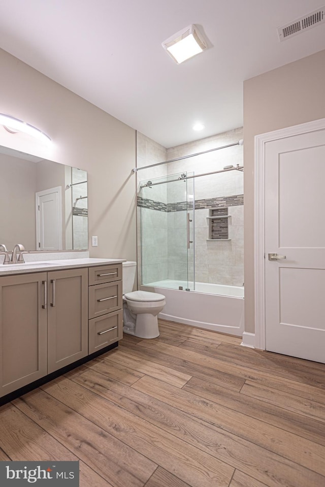 full bathroom with wood-type flooring, bath / shower combo with glass door, toilet, and vanity