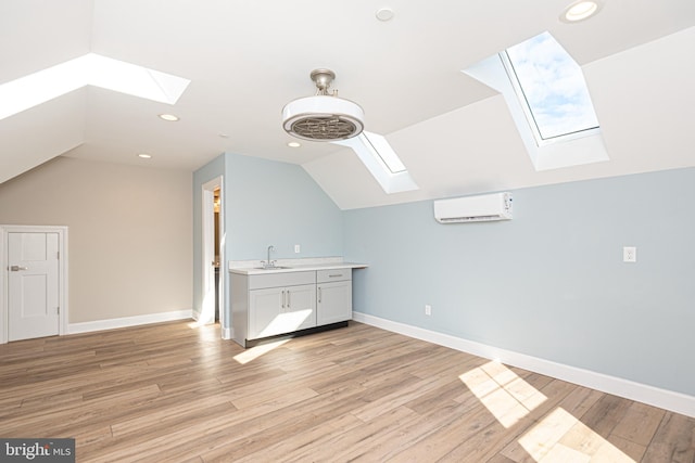 additional living space featuring lofted ceiling with skylight, sink, light hardwood / wood-style flooring, and a wall unit AC