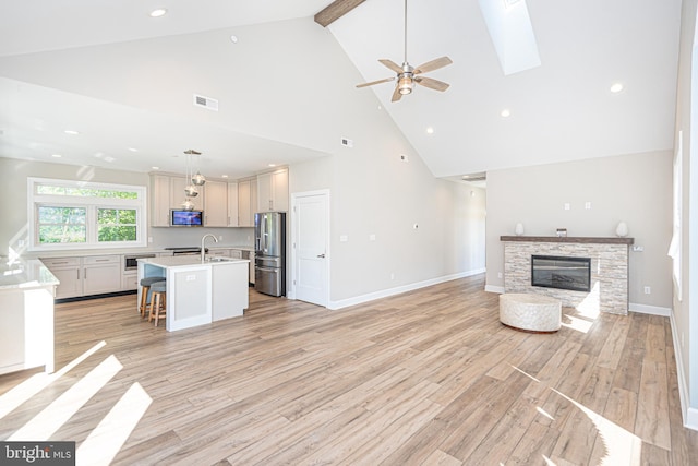 kitchen with pendant lighting, a breakfast bar area, an island with sink, stainless steel refrigerator with ice dispenser, and ceiling fan