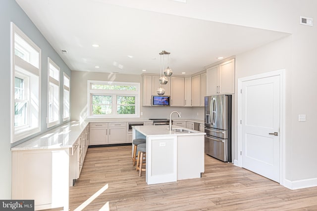 kitchen featuring sink, decorative light fixtures, a center island with sink, stainless steel fridge with ice dispenser, and light wood-type flooring