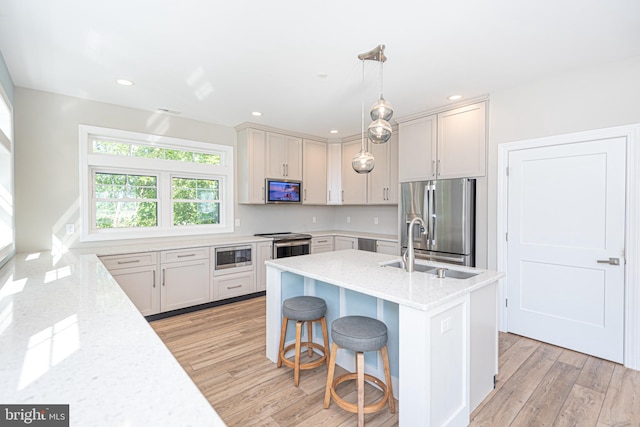 kitchen with appliances with stainless steel finishes, light hardwood / wood-style floors, light stone counters, and decorative light fixtures