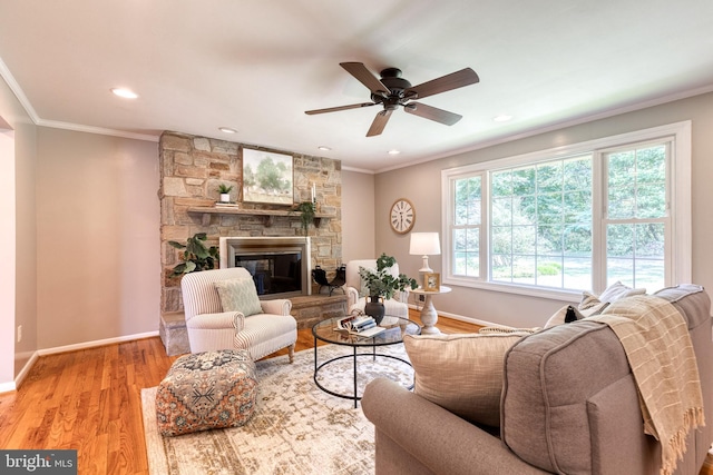 living room featuring ceiling fan, a stone fireplace, light wood-type flooring, and ornamental molding