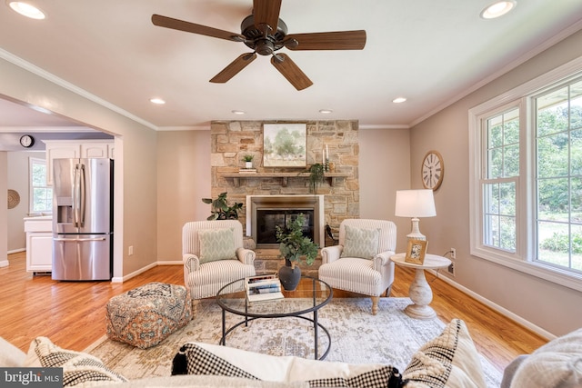 living room featuring a fireplace, ornamental molding, ceiling fan, and light hardwood / wood-style flooring