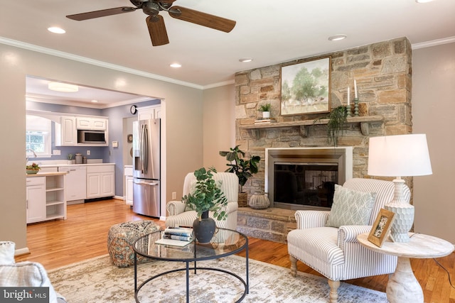 living room with a stone fireplace, crown molding, light hardwood / wood-style floors, and ceiling fan