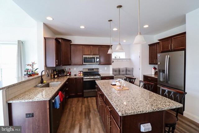 kitchen with decorative light fixtures, stainless steel appliances, dark hardwood / wood-style flooring, sink, and a kitchen bar