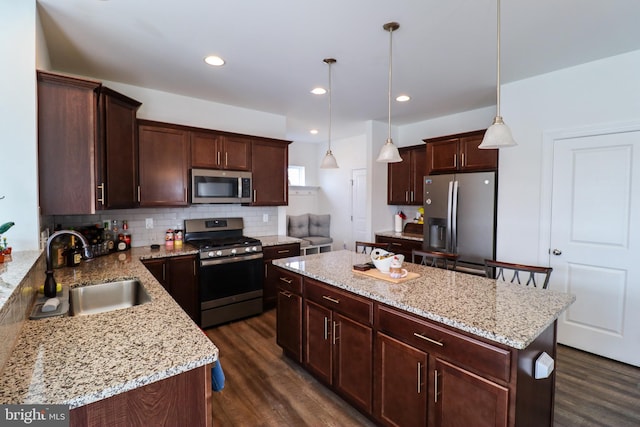 kitchen featuring decorative light fixtures, appliances with stainless steel finishes, sink, dark wood-type flooring, and a kitchen island