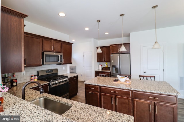 kitchen featuring appliances with stainless steel finishes, light stone countertops, dark hardwood / wood-style flooring, sink, and pendant lighting