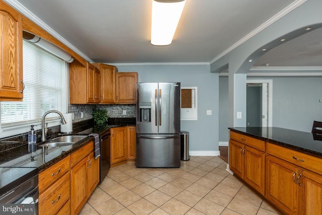 kitchen featuring dark stone countertops, dishwasher, sink, stainless steel fridge, and ornamental molding