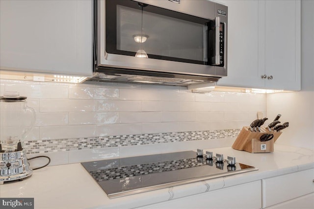 interior details with stainless steel microwave, white cabinets, light countertops, decorative backsplash, and black electric stovetop