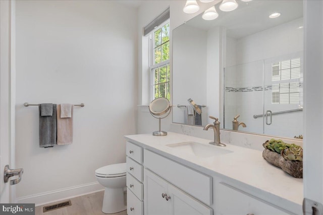 bathroom featuring a shower with shower door, visible vents, toilet, baseboards, and vanity