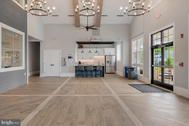 interior space with baseboards, high vaulted ceiling, ceiling fan with notable chandelier, and light wood finished floors