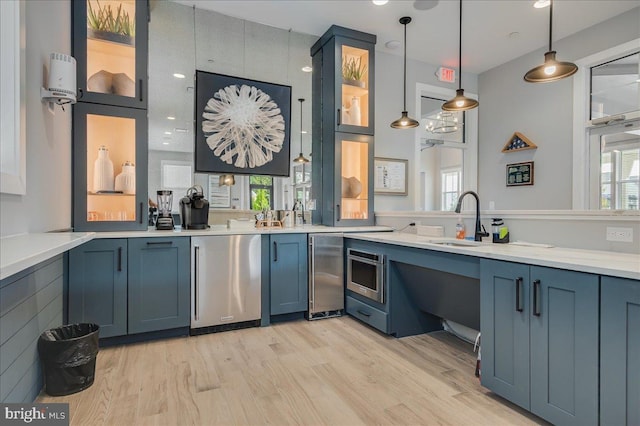 kitchen with refrigerator, blue cabinetry, light wood finished floors, and a sink