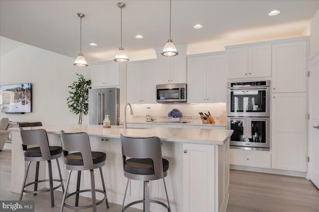 kitchen with tasteful backsplash, a center island with sink, light countertops, appliances with stainless steel finishes, and a sink