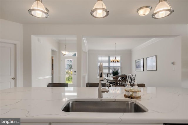 kitchen featuring hanging light fixtures, crown molding, light stone counters, and a sink