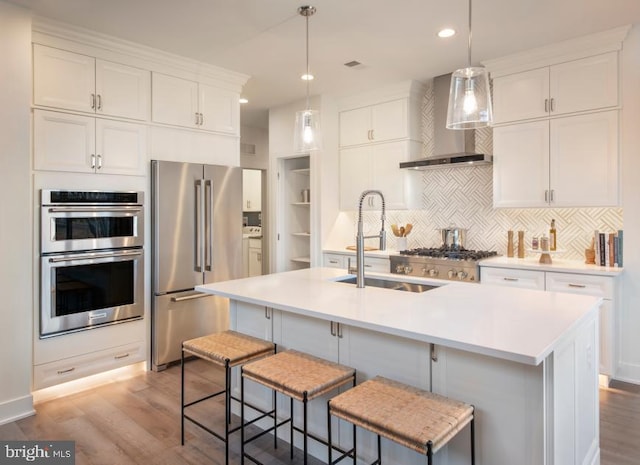 kitchen with a sink, stainless steel appliances, light wood-style floors, and wall chimney exhaust hood