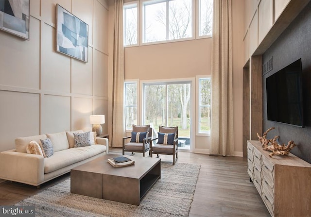 living room featuring visible vents, a high ceiling, wood finished floors, and a decorative wall