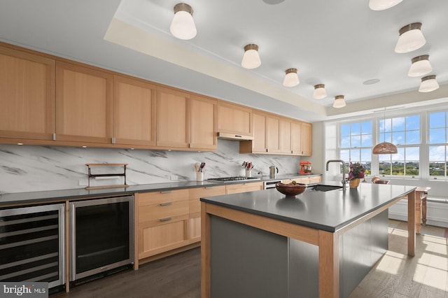 kitchen featuring an island with sink, dark wood-type flooring, beverage cooler, and stainless steel gas stovetop