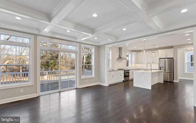 kitchen featuring an island with sink, wall chimney range hood, stainless steel appliances, decorative light fixtures, and dark hardwood / wood-style flooring