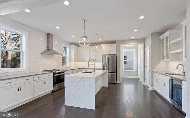 kitchen featuring appliances with stainless steel finishes, wall chimney exhaust hood, beverage cooler, a kitchen island with sink, and sink