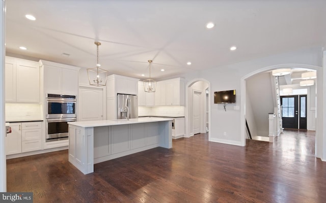 kitchen featuring white cabinets, an island with sink, hanging light fixtures, stainless steel appliances, and dark hardwood / wood-style floors