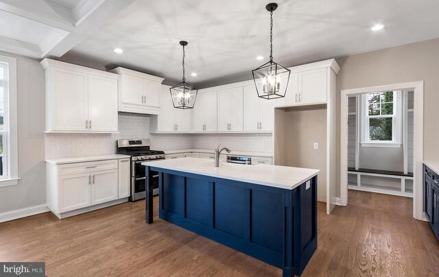 kitchen featuring white cabinets, hanging light fixtures, stainless steel range with gas stovetop, wood-type flooring, and backsplash