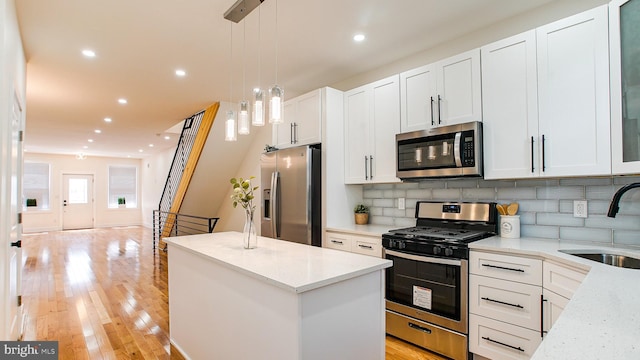 kitchen featuring a kitchen island, stainless steel appliances, sink, light stone counters, and light wood-type flooring