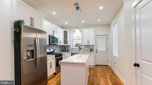 kitchen featuring an island with sink, stainless steel appliances, white cabinets, and light hardwood / wood-style floors