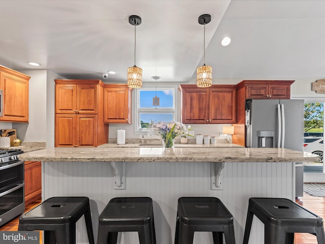 kitchen with appliances with stainless steel finishes, wood-type flooring, light stone countertops, and a kitchen breakfast bar