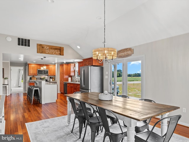 dining space with light hardwood / wood-style flooring, vaulted ceiling, sink, and a chandelier