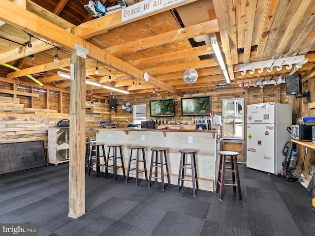 kitchen with wood walls, white fridge, a kitchen breakfast bar, and dark colored carpet