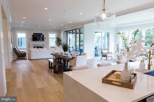 kitchen featuring light wood-type flooring, crown molding, a wealth of natural light, and decorative light fixtures