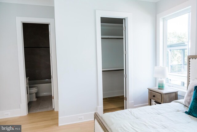 bedroom featuring light hardwood / wood-style flooring, a spacious closet, ensuite bathroom, and multiple windows