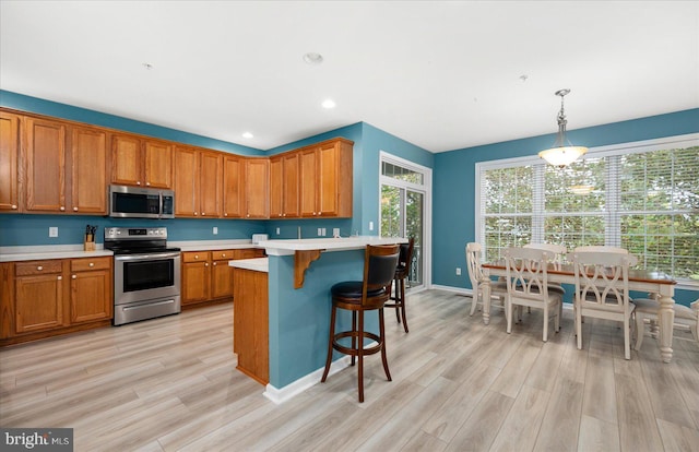 kitchen with light countertops, a kitchen breakfast bar, light wood-style floors, brown cabinetry, and stainless steel appliances