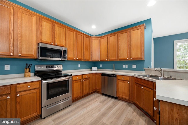 kitchen with brown cabinetry, light wood-style flooring, a sink, stainless steel appliances, and light countertops